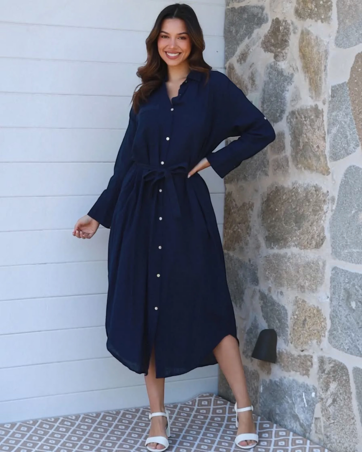 A woman wearing a Thrift N Gift navy blue midi shirt dress with a tie-waist, long sleeves, and white strappy heels.