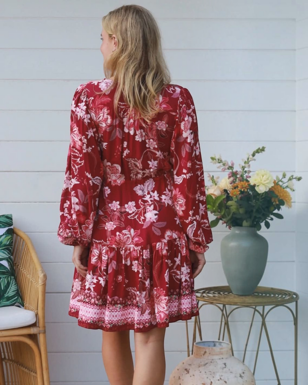 Back view of a woman wearing a Thrift N Gift red floral print long sleeve mini dress with a tiered skirt.