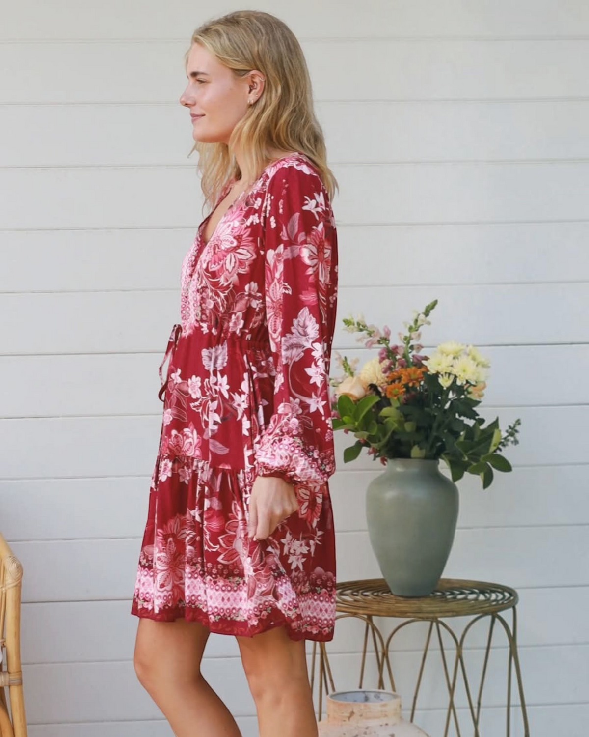 Thrift N Gift long sleeve mini dress in deep red with a floral print, V-neck, and tiered skirt, side profile view.