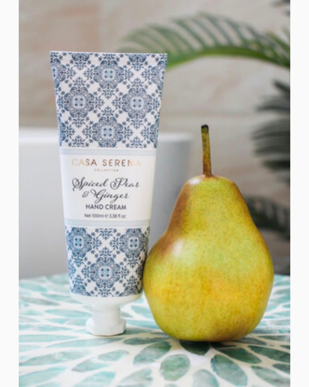 Thrift N Gift Casa Serena Spiced Pear and Ginger hand cream tube with blue patterned design next to a fresh pear